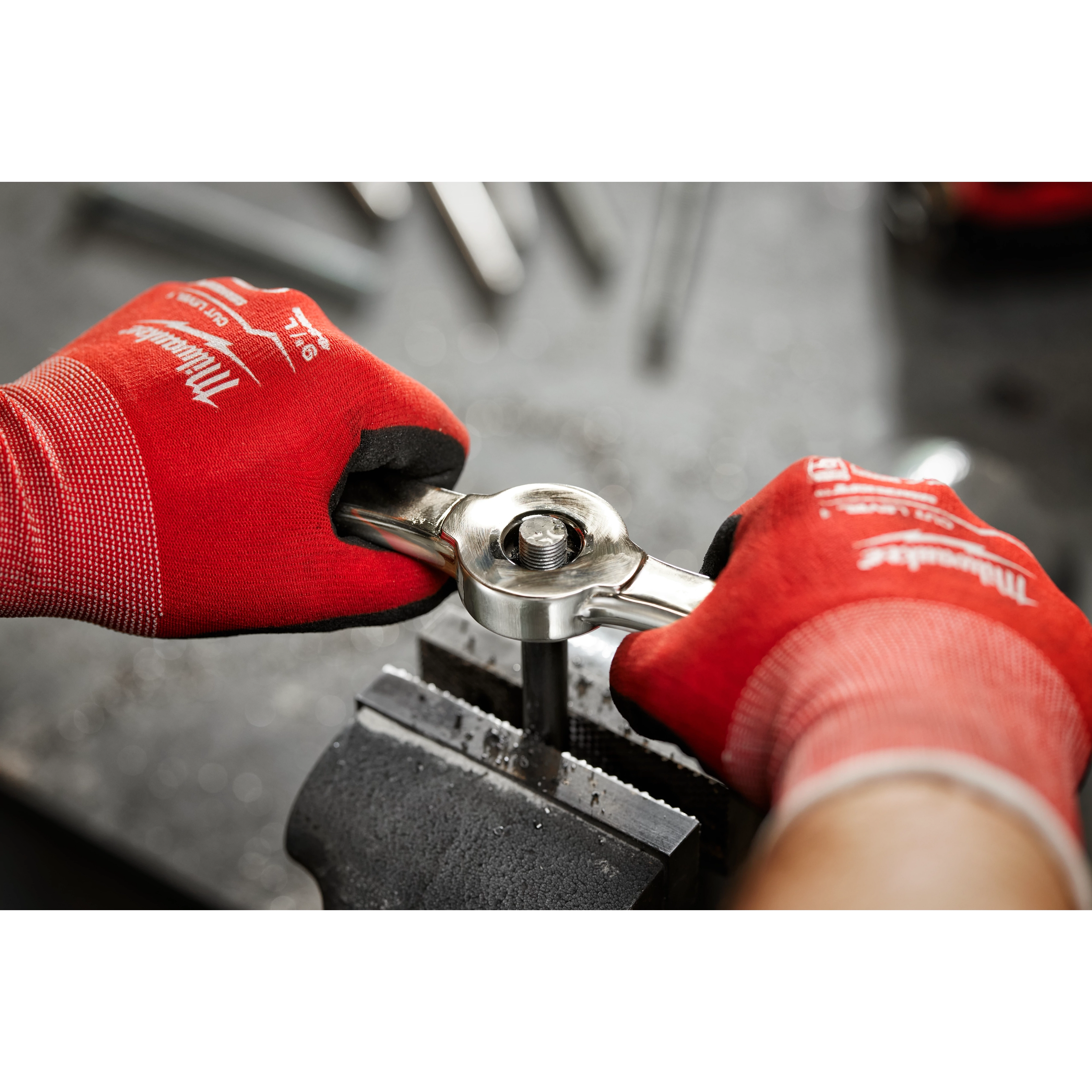 A person wearing red gloves is using the Hex-LOK™ 2-in-1 Threading Handle to thread a metal rod that is secured in a vise.