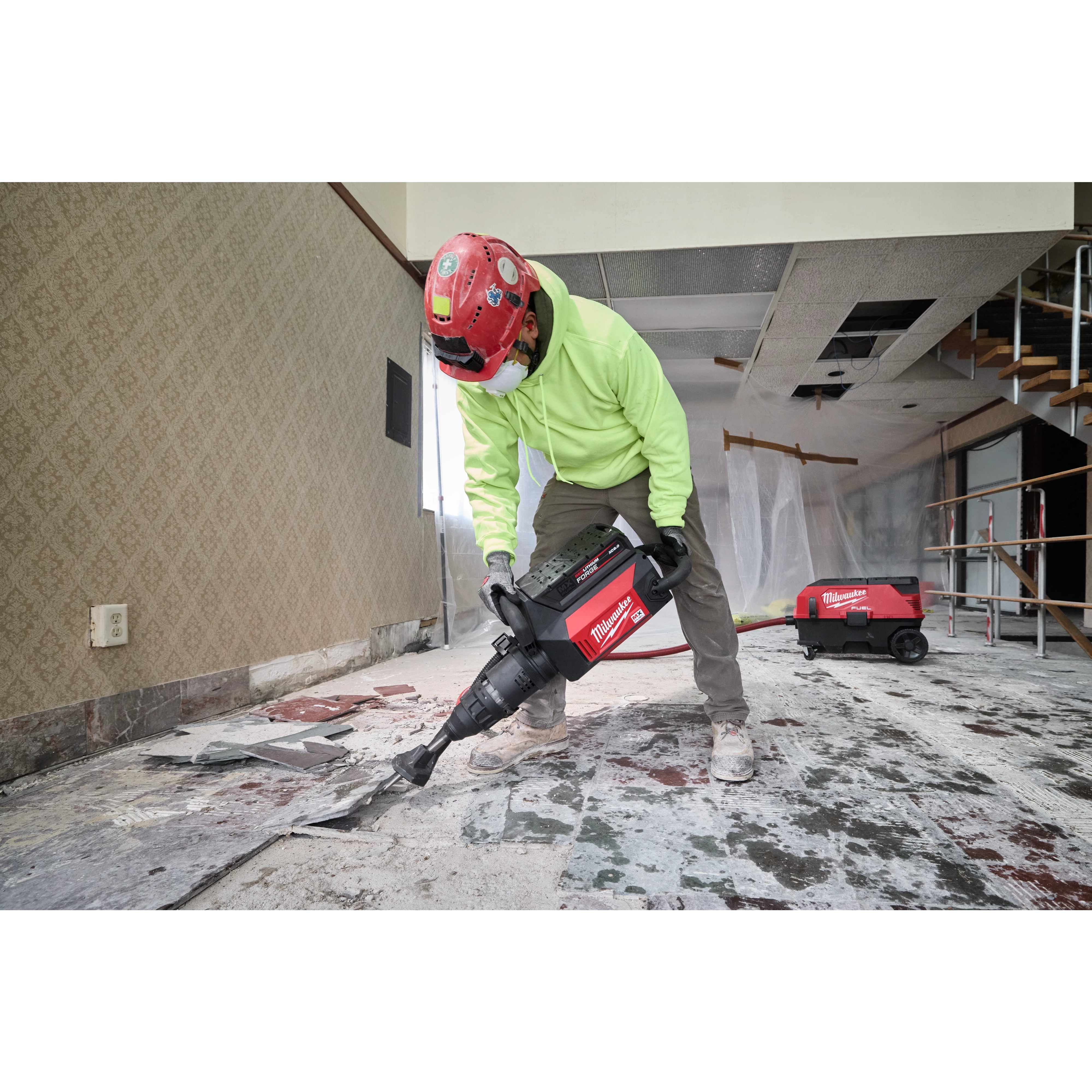 A construction worker uses the MX FUEL 27 lb SDS MAX Demolition Hammer to remove floor tiles in a partially renovated room.