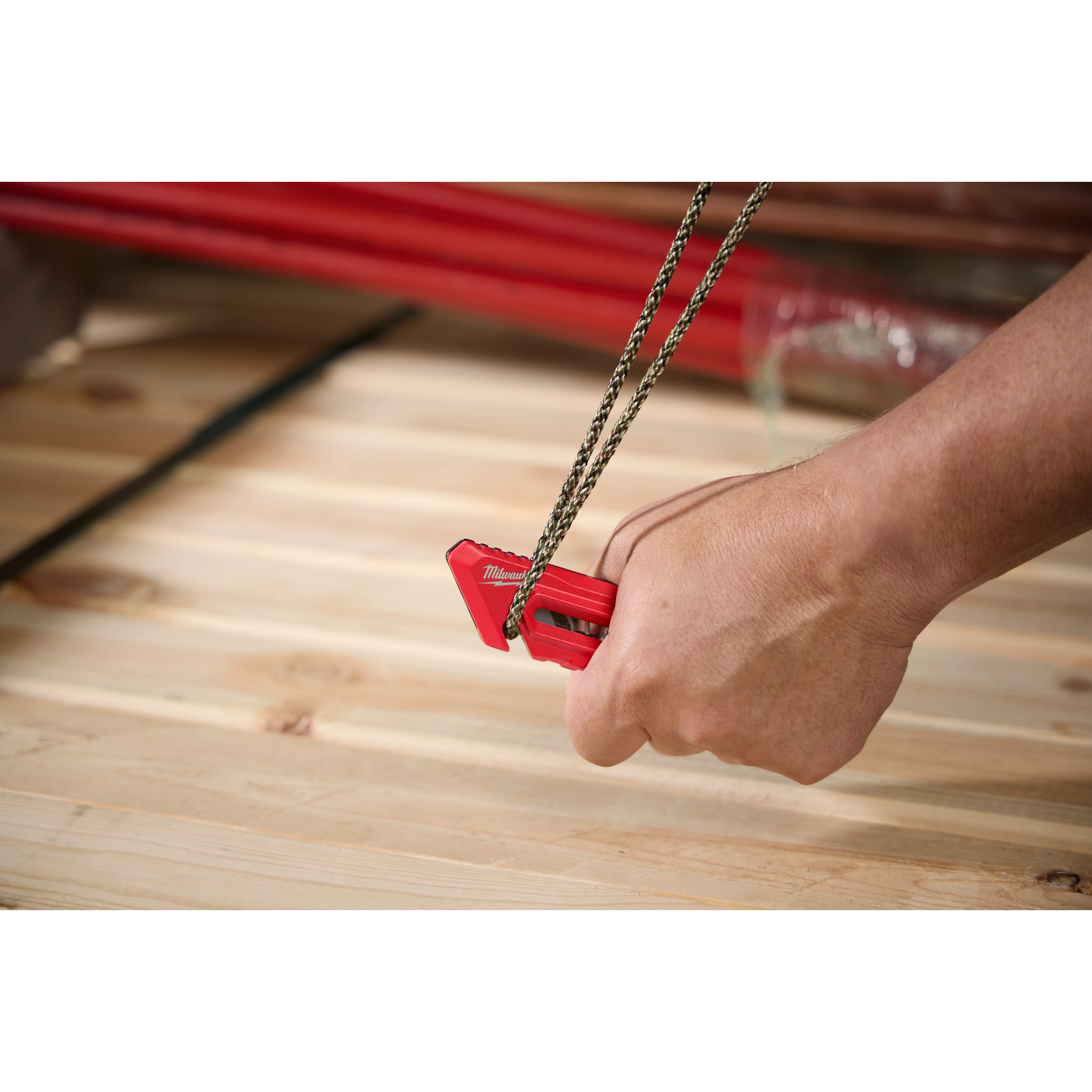 A hand using the Multi-function Compact Utility Knife to cut a piece of rope on a wooden surface. The small, red utility knife is held firmly, demonstrating its capability to slice through durable material efficiently.